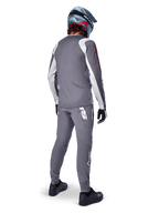 Alpinestars A-Supra Astar Jersey, MTB-jersey met lange mouwen, donkergrijs met witte mouwaccenten en rood logo, achteraanzicht van een rijder met bijpassende grijze broek en blauwe full-face helm, hoogwaardige fietskleding