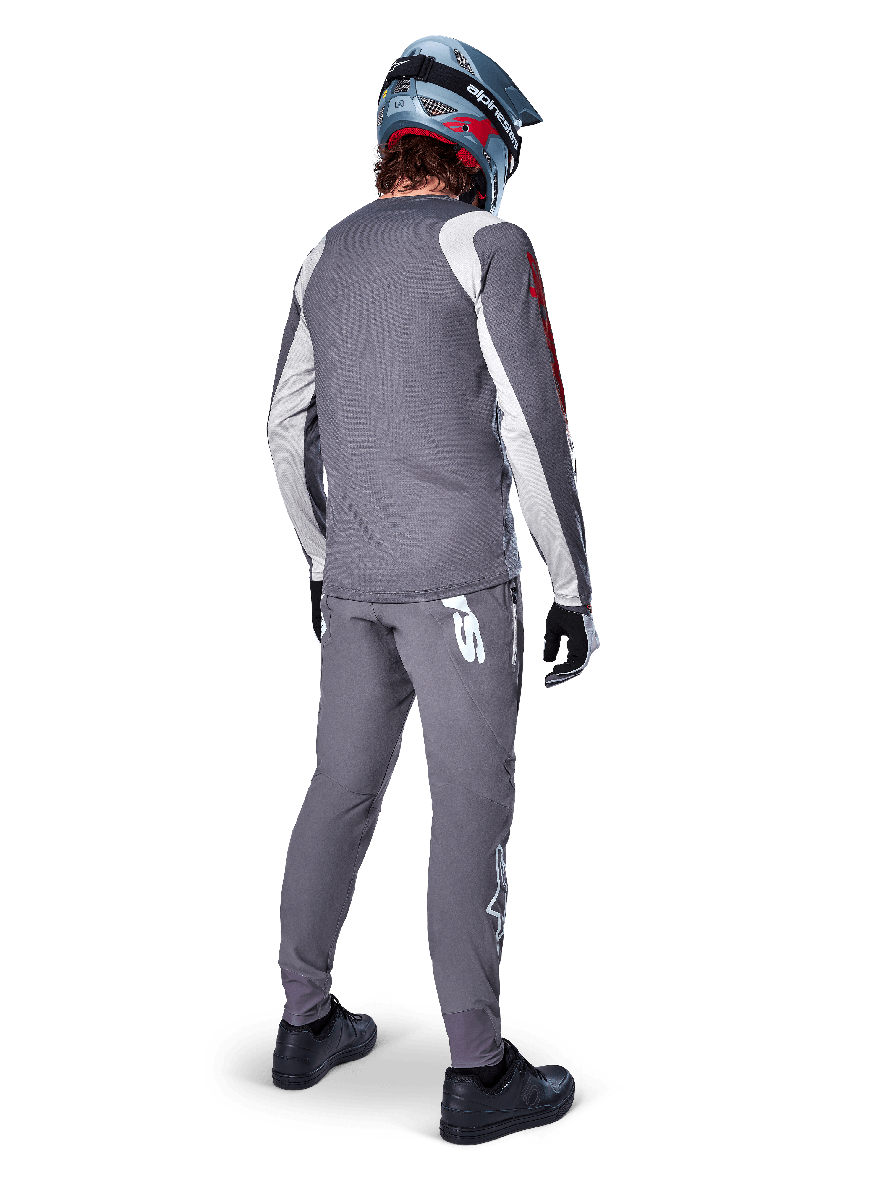 Alpinestars A-Supra Astar Jersey, MTB-jersey met lange mouwen, donkergrijs met witte mouwaccenten en rood logo, achteraanzicht van een rijder met bijpassende grijze broek en blauwe full-face helm, hoogwaardige fietskleding