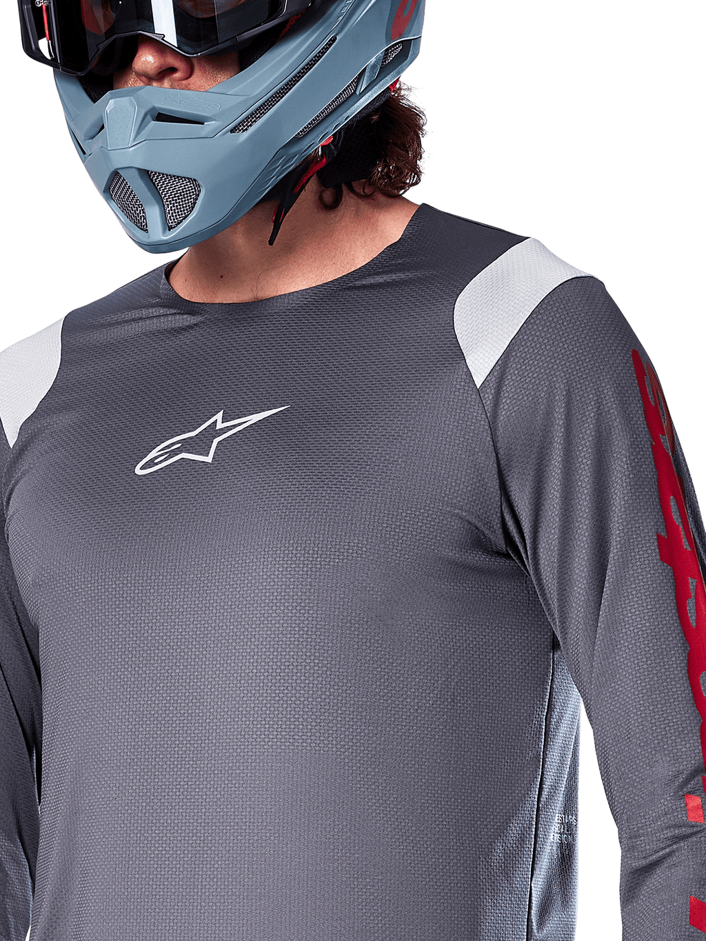 Alpinestars A-Supra Astar Jersey met lange mouwen, donkergrijs met witte schouderpanelen en rode graphics op de mouwen, gedragen met een licht blauwgrijze full-face helm, performance mountainbikekleding