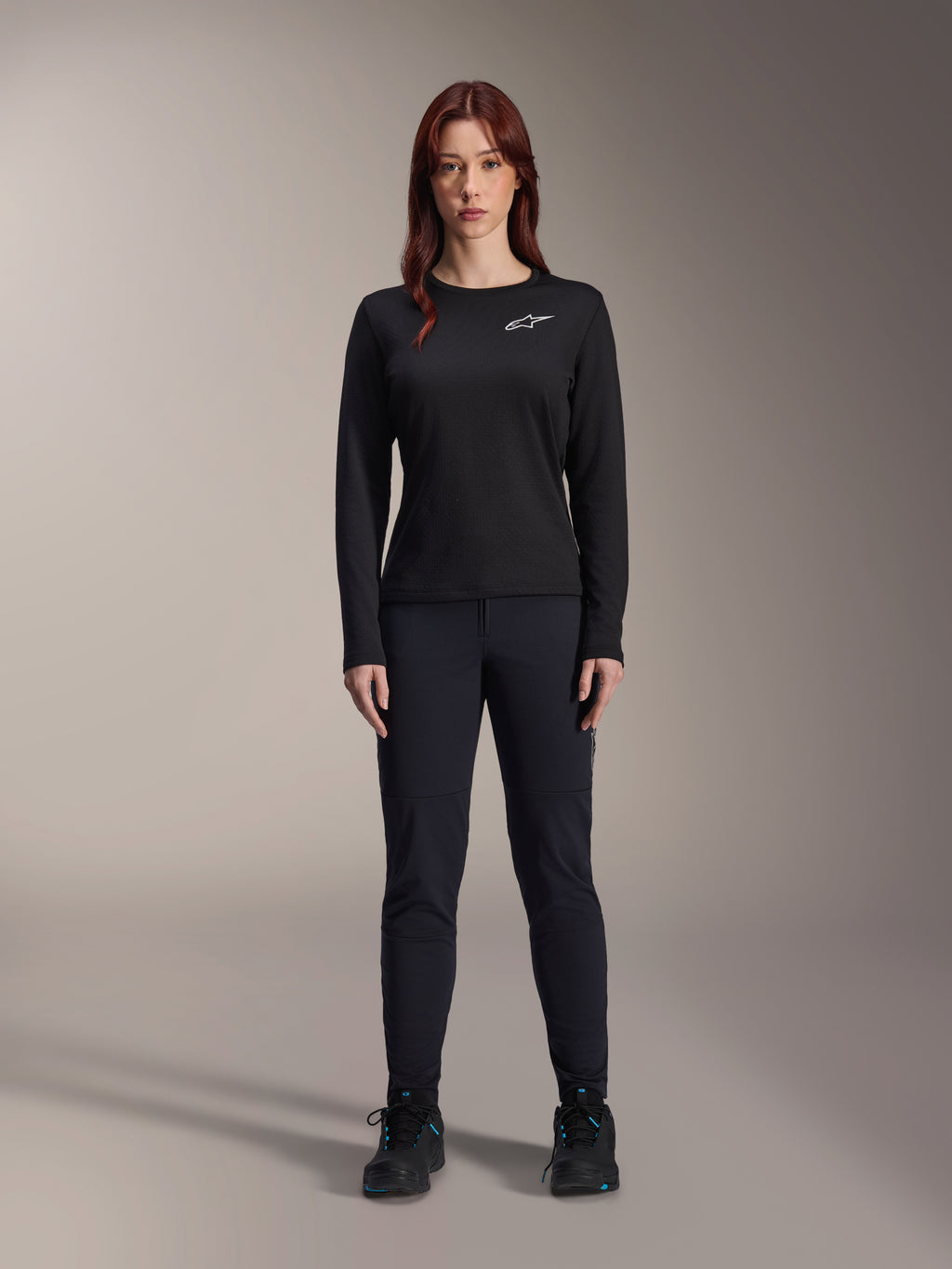 Alpinestars Stella A-Dura Thermal Jersey, dames mountainbike jersey met lange mouwen in het zwart, voorzien van een wit logo op de borst, gedragen met bijpassende zwarte uitrusting en fietsschoenen, studioportret.