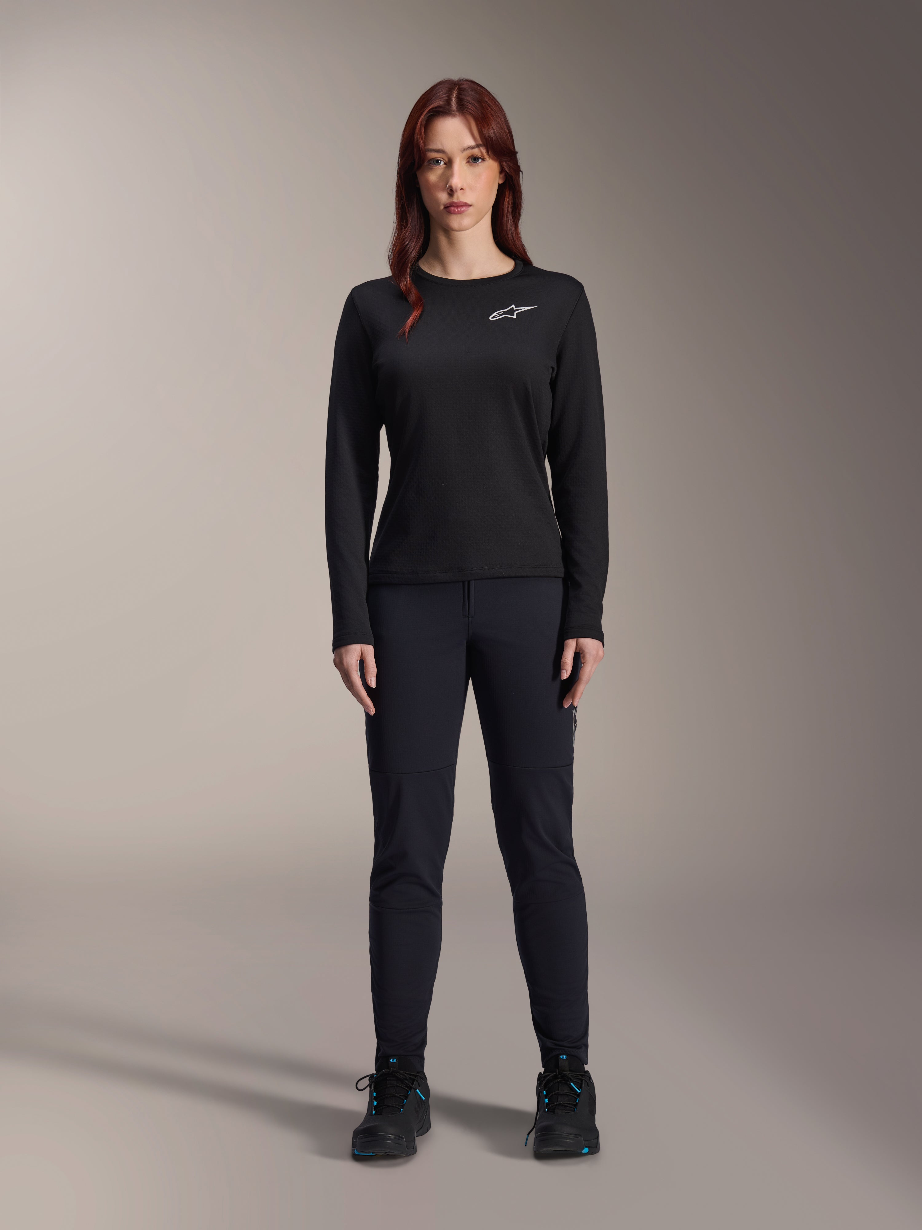 Alpinestars Stella A-Dura Thermal Jersey, dames mountainbike jersey met lange mouwen in het zwart, voorzien van een wit logo op de borst, gedragen met bijpassende zwarte uitrusting en fietsschoenen, studioportret.