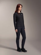 Vrouw die de Alpinestars Stella A-Dura Thermal Jersey draagt, zwart MTB-shirt met lange mouwen en wit logo op de borst, gestyled met bijpassende zwarte broek en sportschoenen, studioportret voor technische wielerkleding