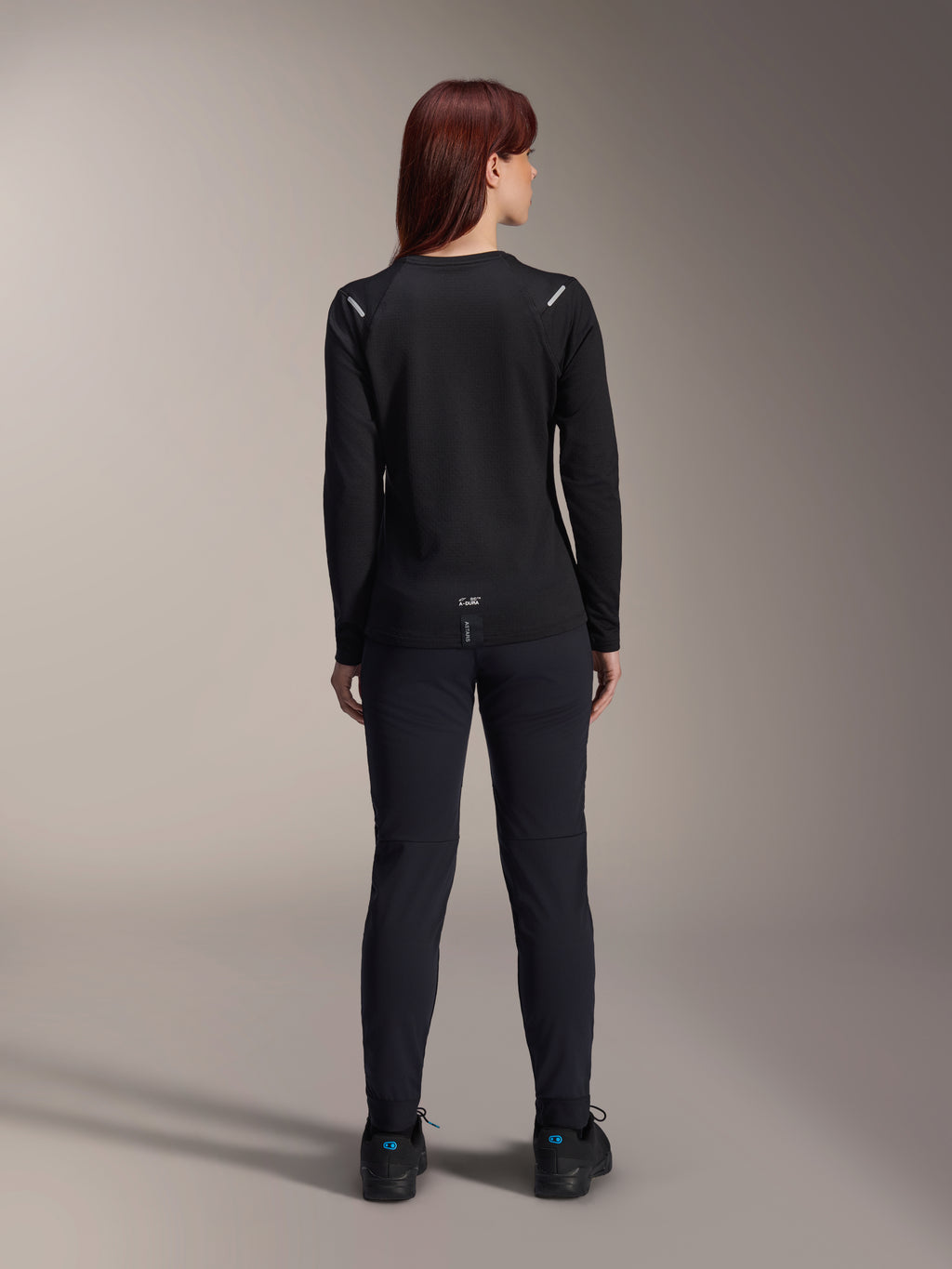 Alpinestars Stella A-Dura Thermal Jersey voor dames, achteraanzicht, zwart, fietsshirt met lange mouwen en geïsoleerd fleece, gedragen met bijpassende zwarte broek en schoenen, met kleine A-Dura branding op de onderrug en reflecterende schouderaccenten, speciaal ontworpen voor MTB-ritten voor dames.