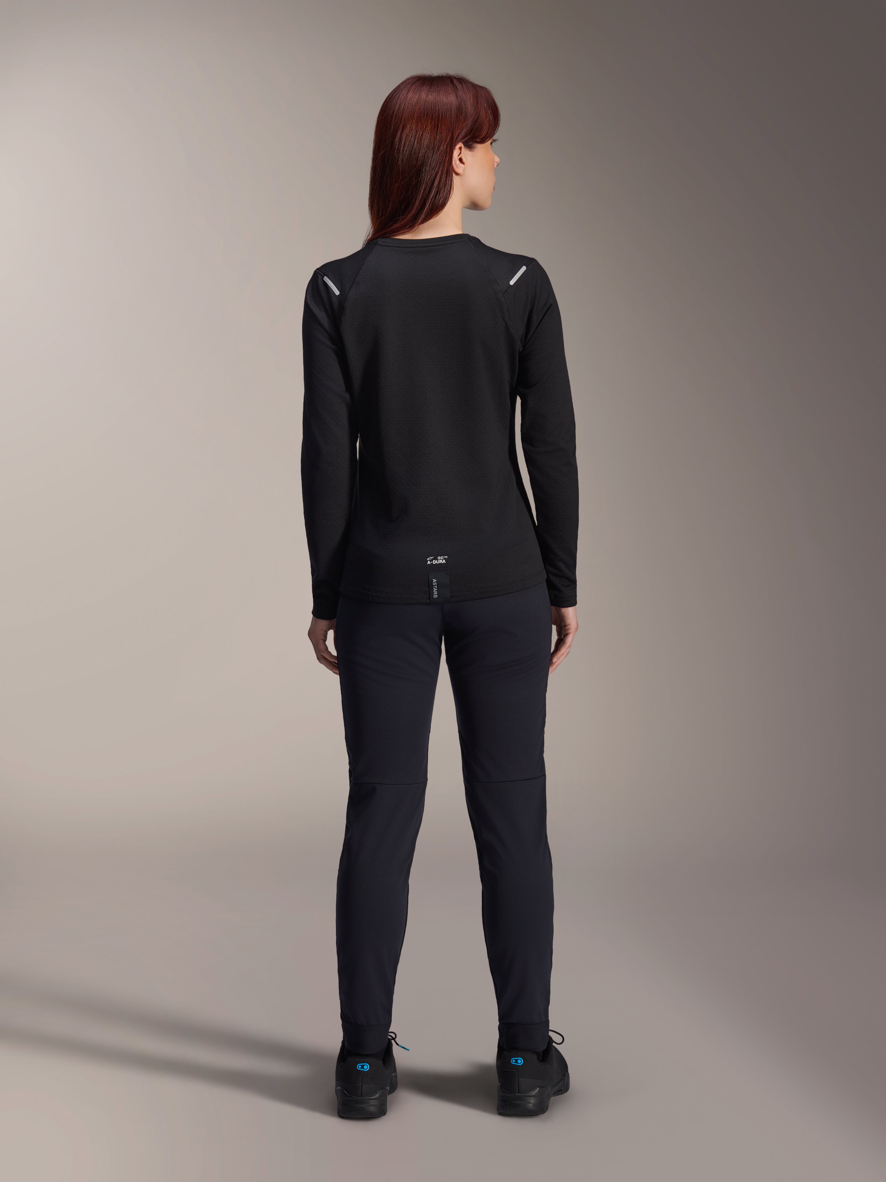 Alpinestars Stella A-Dura Thermal Jersey voor dames, achteraanzicht, zwart, fietsshirt met lange mouwen en geïsoleerd fleece, gedragen met bijpassende zwarte broek en schoenen, met kleine A-Dura branding op de onderrug en reflecterende schouderaccenten, speciaal ontworpen voor MTB-ritten voor dames.