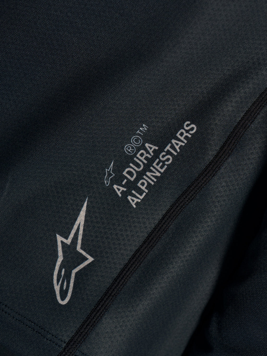 Détail du maillot Stella A-Dura Ride noir, tissu jacquard technique avec logos A-DURA ALPINESTARS et Astars.