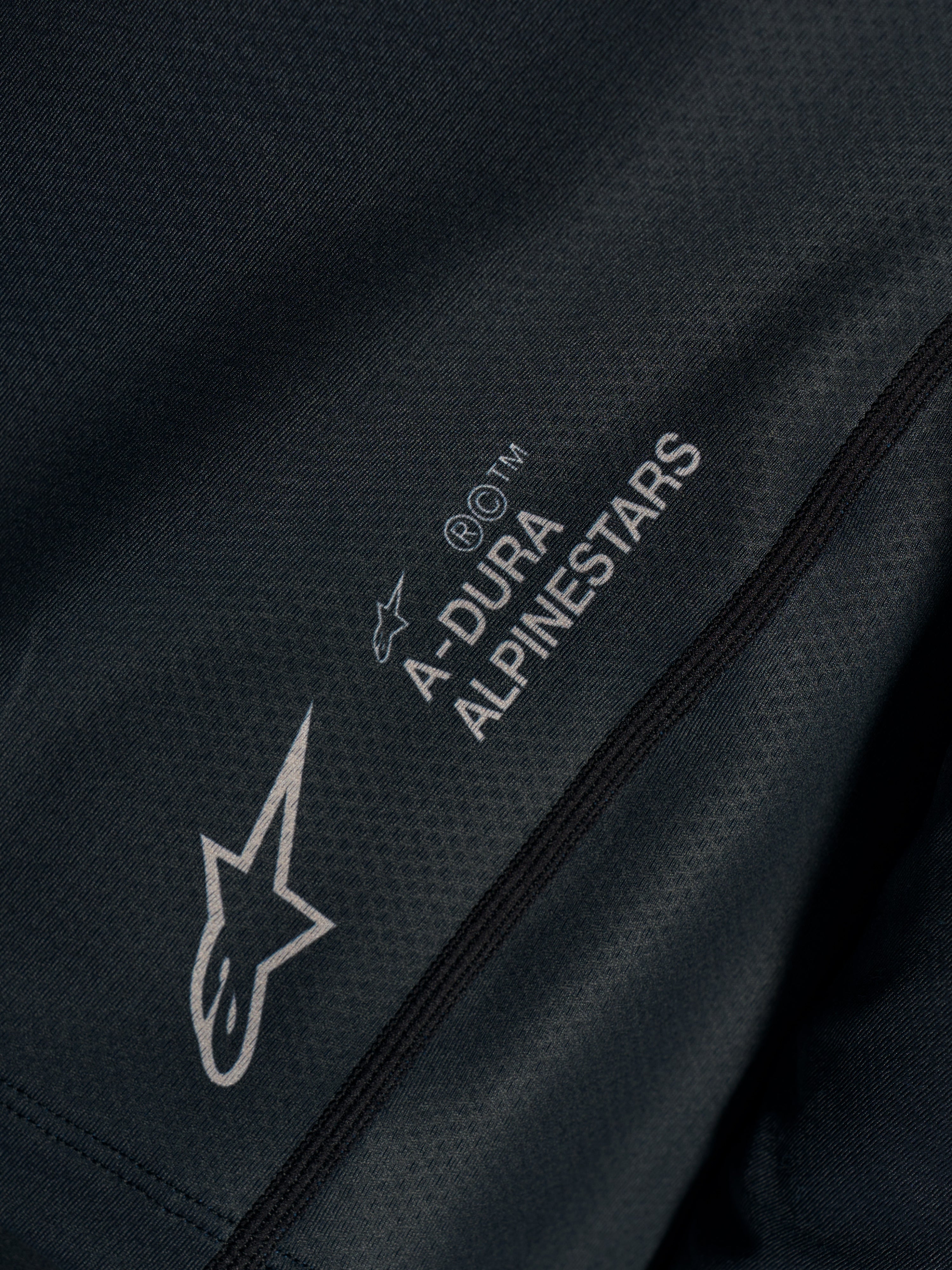 Détail du maillot Stella A-Dura Ride noir, tissu jacquard technique avec logos A-DURA ALPINESTARS et Astars.
