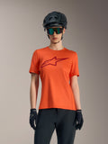 Maillot orange Stella A-Dura Ride femme à manches courtes, logo rouge, avec casque de VTT et lunettes noirs.