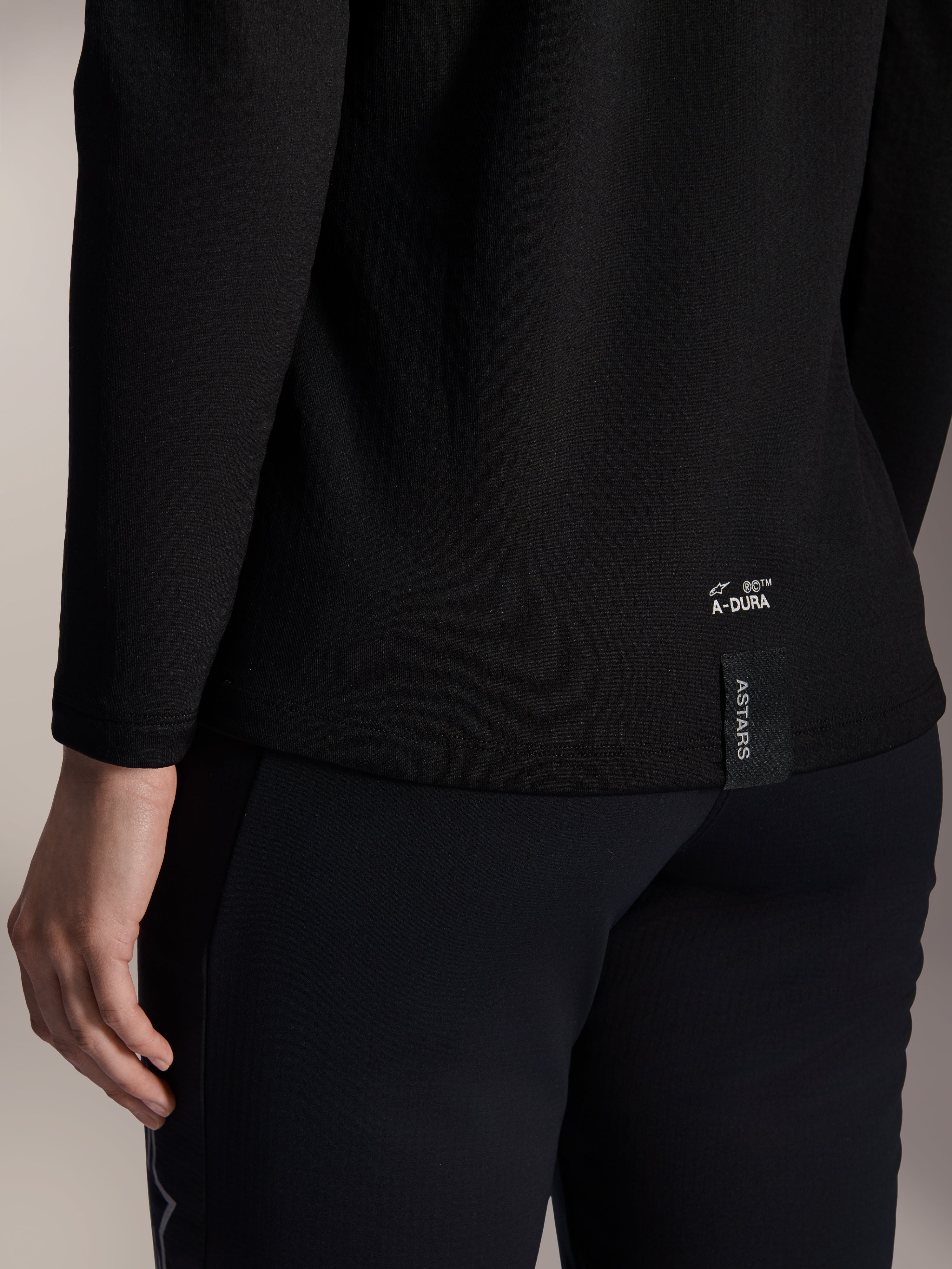 Alpinestars Stella A-Dura Thermal Jersey voor dames, zwart thermisch MTB-shirt, close-up van de onderste zoom aan de achterkant met witte A-DURA-branding en verticaal ASTARS-logolabel, ontworpen voor mountainbiken in koud weer