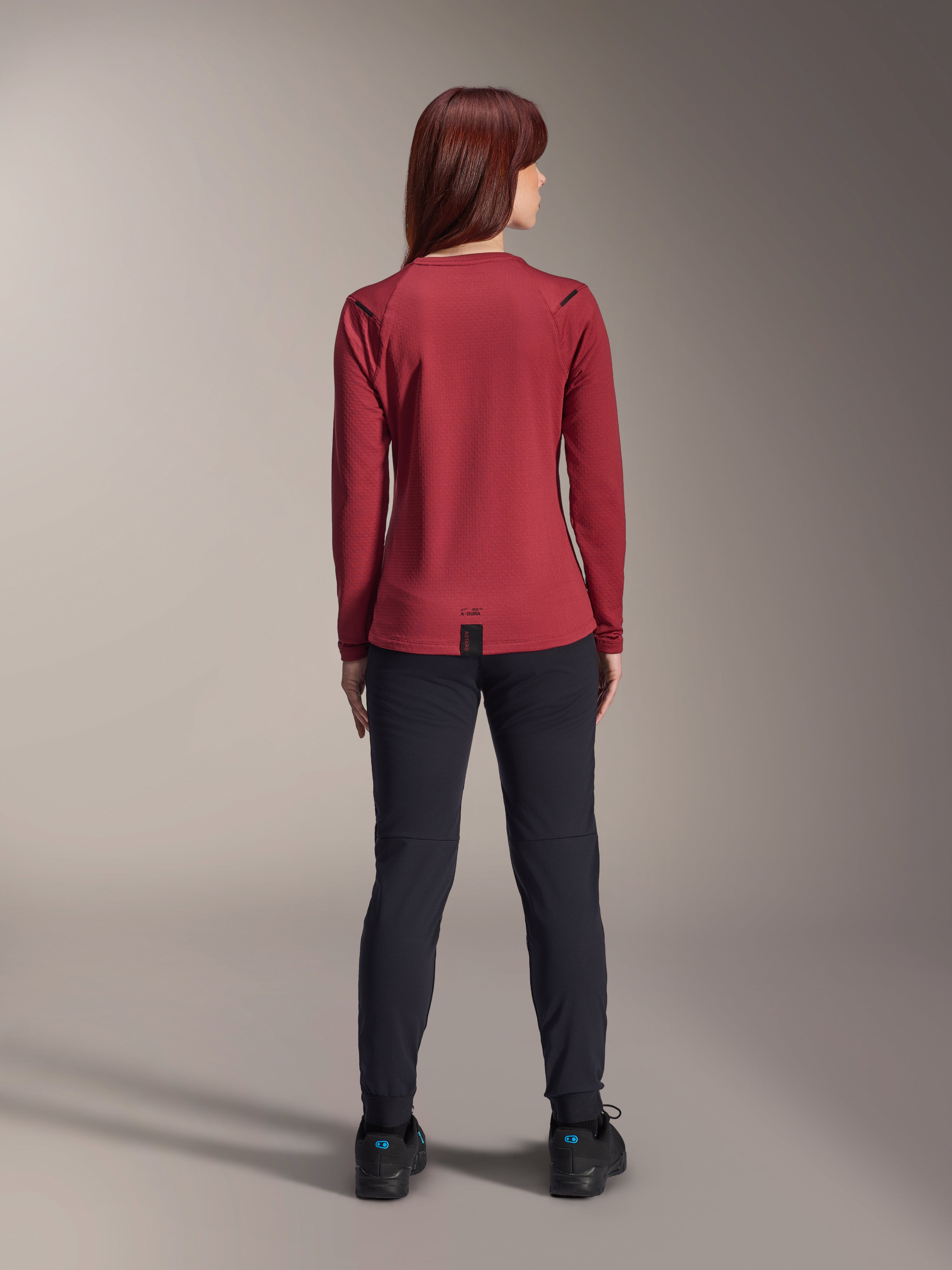Pantalon thermique Alpinestars Stella A-Dura, pantalon de VTT pour femme, noir, porté avec un maillot thermique bordeaux à manches longues, vue de dos montrant la coupe technique et la construction pour le cyclisme par temps froid.