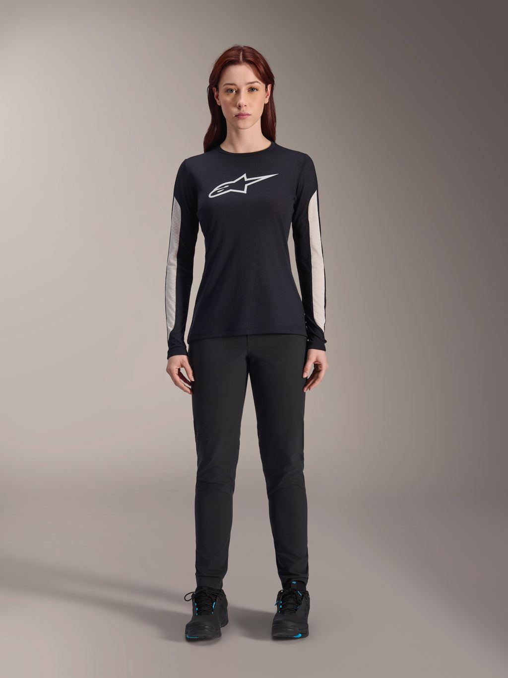 Frau im Alpinestars Stella A-Dura Dri Astar Langarmtrikot, Schwarz mit weißem Brustlogo und hellen Mesh-Ärmeleinsätzen, kombiniert mit schwarzer Hose und schwarzen Schuhen, technische Mountainbike-Bekleidung