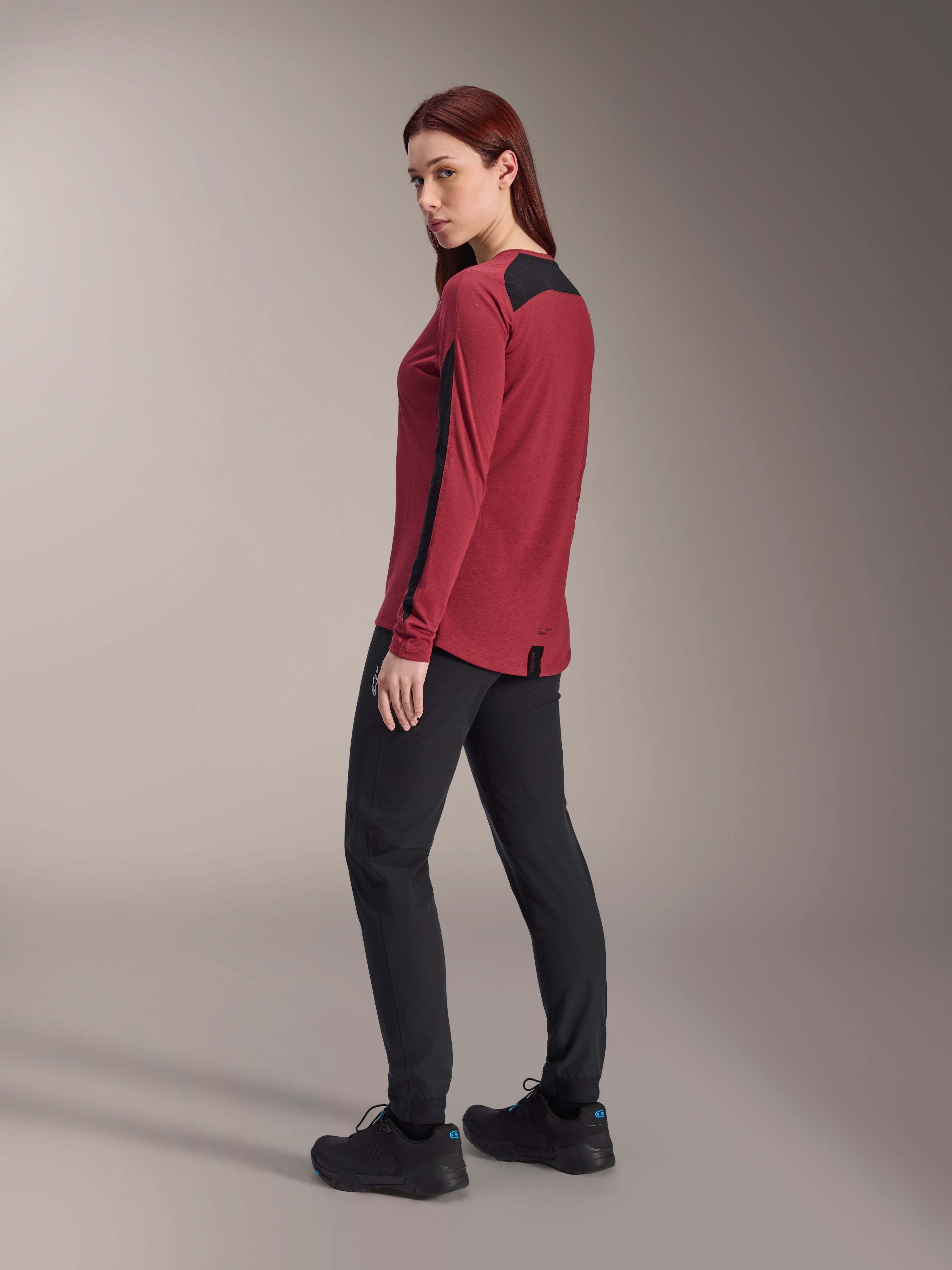 Maillot à manches longues Alpinestars Stella A-Dura Dri Astar pour femme, bordeaux et noir, porté avec un pantalon de VTT noir et des chaussures noires, vue de profil arrière, tissu drirelease recyclé avec panneaux en maille, équipement technique de VTT