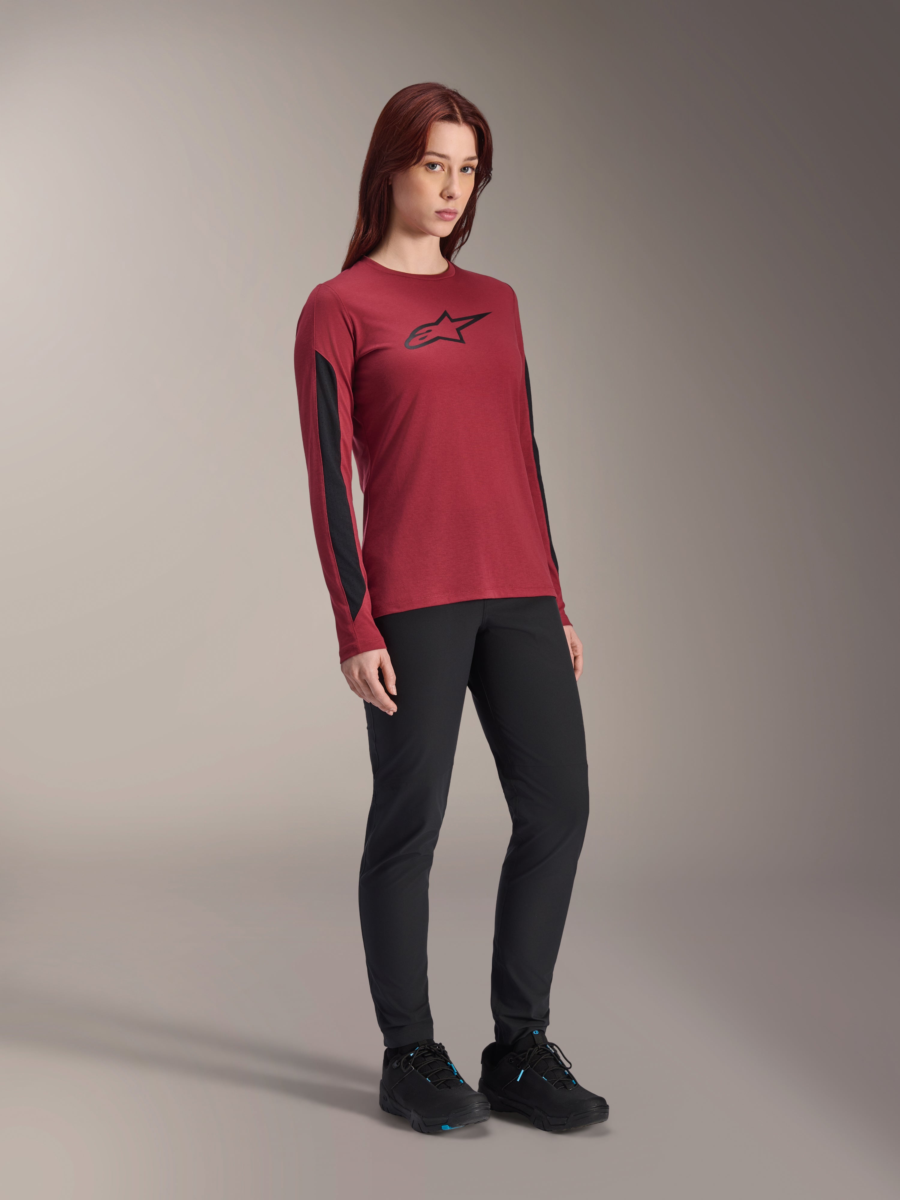 Maillot à manches longues Alpinestars Stella A-Dura Dri Astar pour femme, rouge bordeaux avec logo noir sur la poitrine et empiècements en maille noire sur les manches, porté avec un pantalon technique noir et des chaussures de vélo noires, vêtement de VTT haute performance pour femme