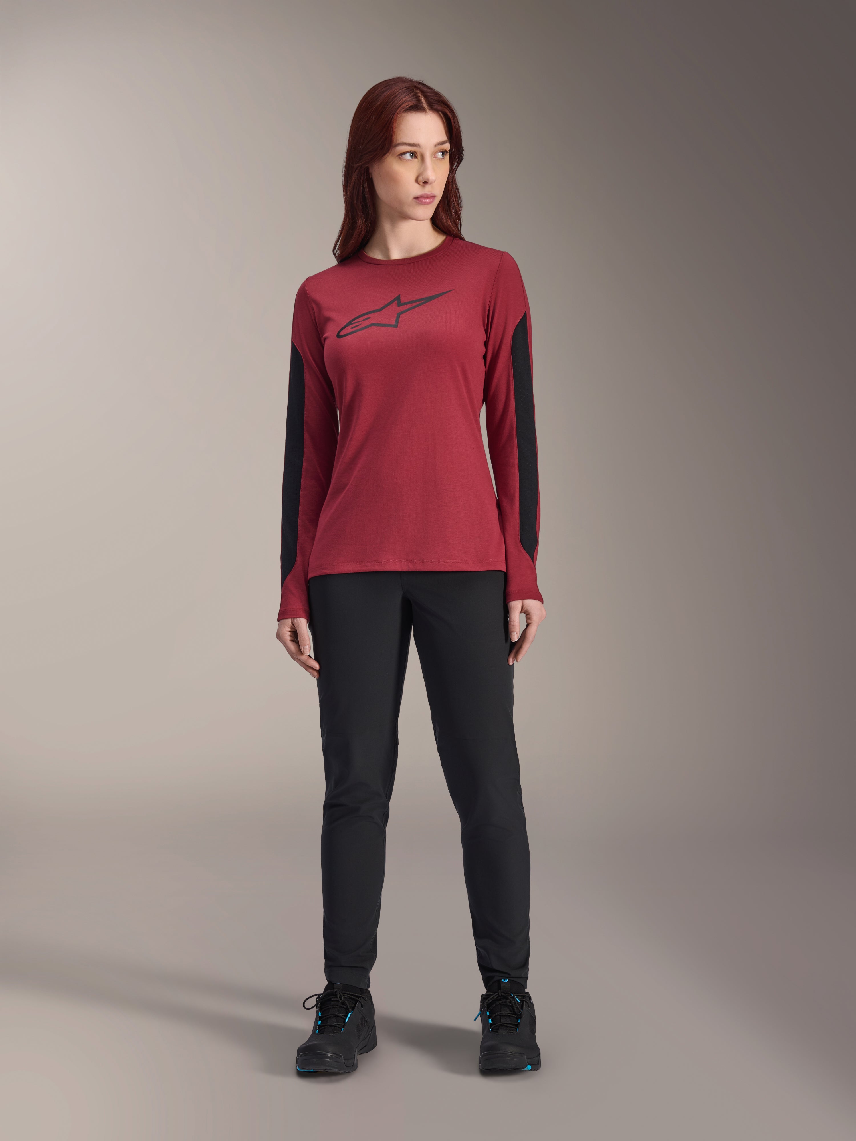 Maillot à manches longues Alpinestars Stella A-Dura Dri Astar pour femme en bordeaux, doté d'un logo Astars noir sur la poitrine et de panneaux en maille noire sur les bras, porté avec un pantalon technique noir et des chaussures de sport, vêtement de VTT de performance pour femme.