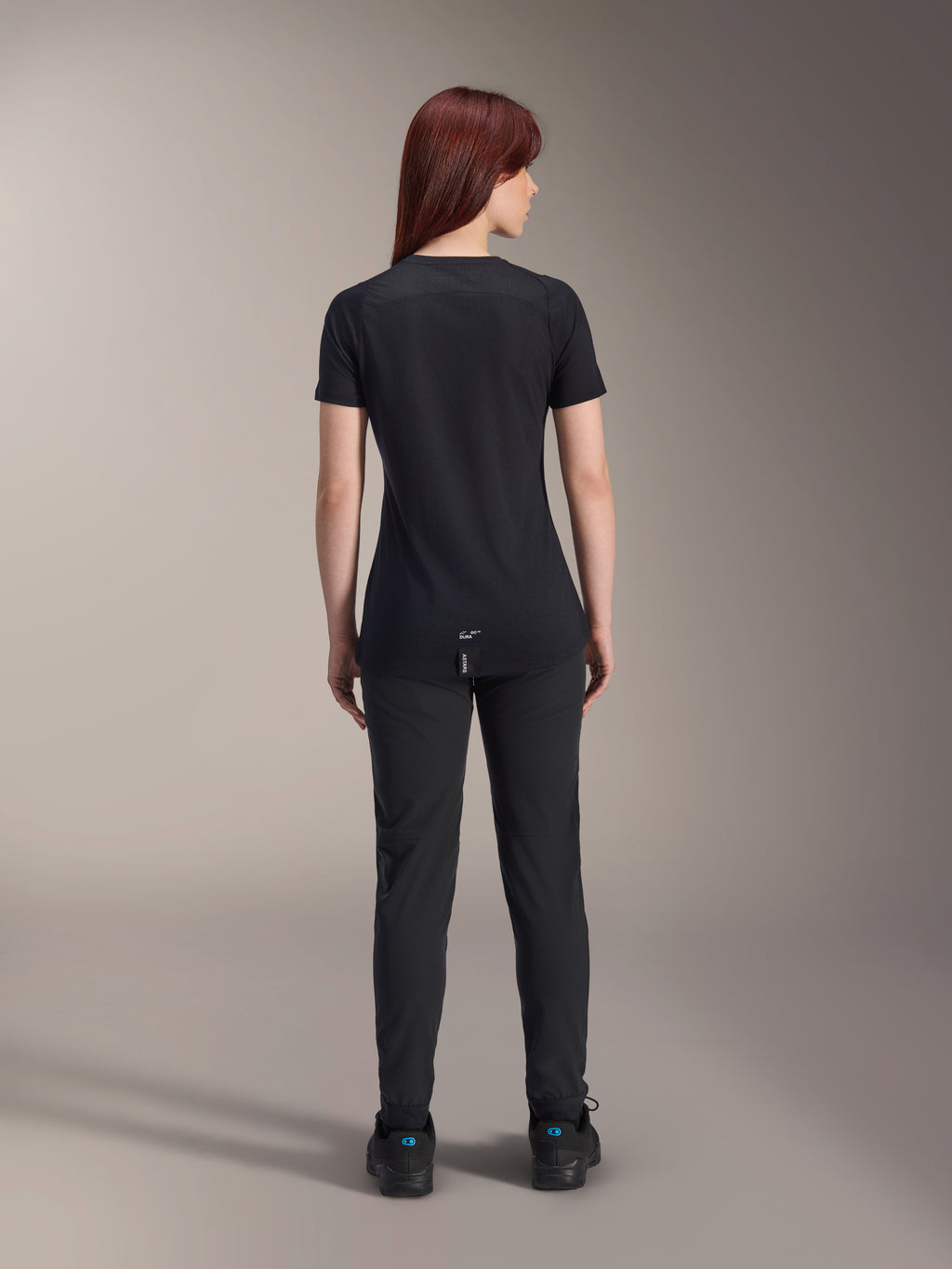 Maillot à manches courtes Alpinestars Stella A-Dura Dri Switch pour femme, noir, vue arrière sur un modèle, avec un pan arrière allongé et des panneaux en maille technique, associé à un pantalon noir, équipement de cyclisme VTT de performance