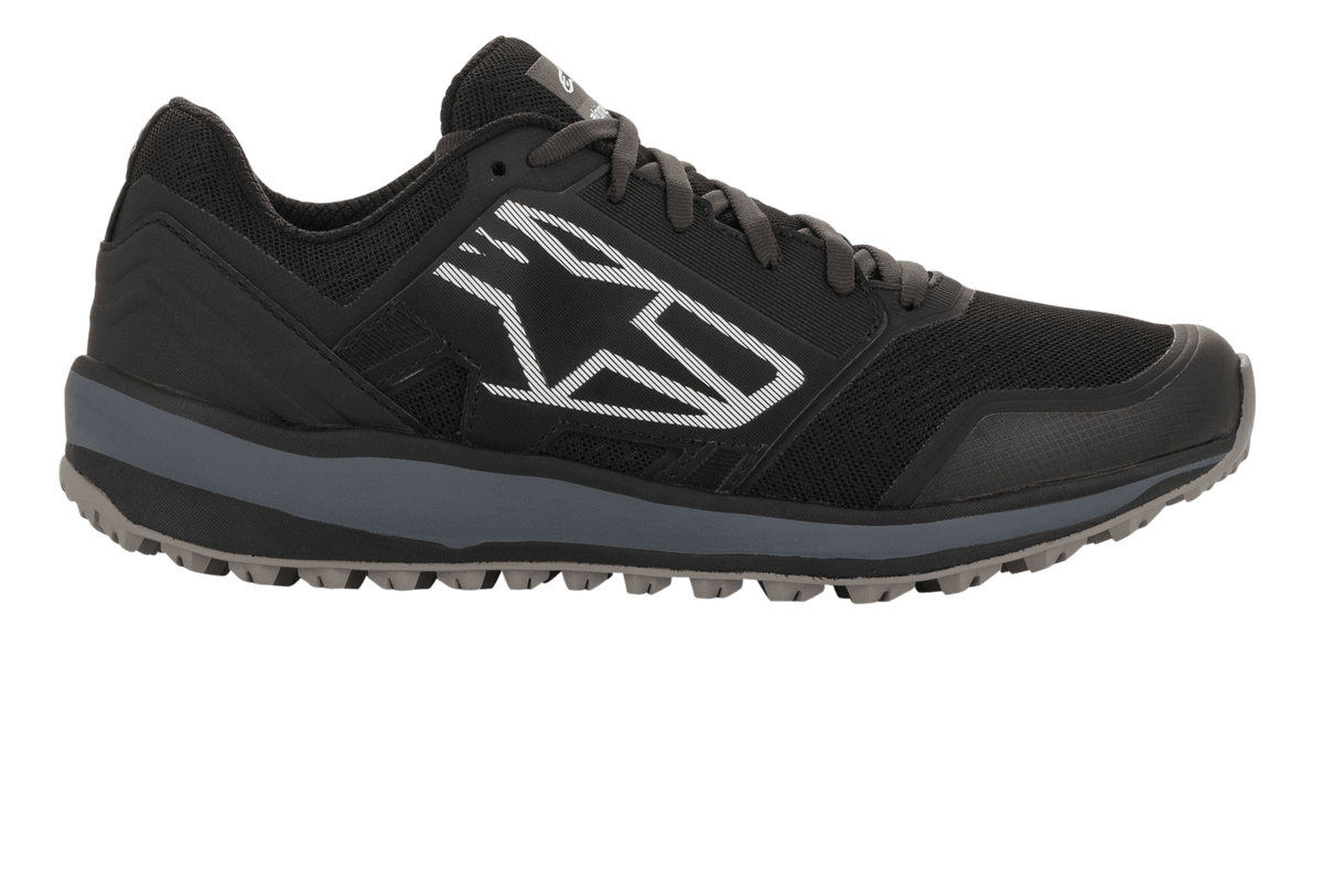 Alpinestars Meta Trail schoenen, performance hardloopschoenen, zwart en donkergrijs, zijprofiel met een groot wit geometrisch Astars-logo, mesh bovenwerk met grijze tussenzool en geprofileerde rubberen zool, casual motorsport paddock-schoeisel