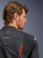 Veste en cuir Alpinestars Dusk Airflow, noir et rouge fluo, gros plan sur le haut du dos et l'épaule, avec cuir perforé pour la ventilation et panneaux extensibles en accordéon, détail du marquage 'DUSK', portée par un mannequin homme