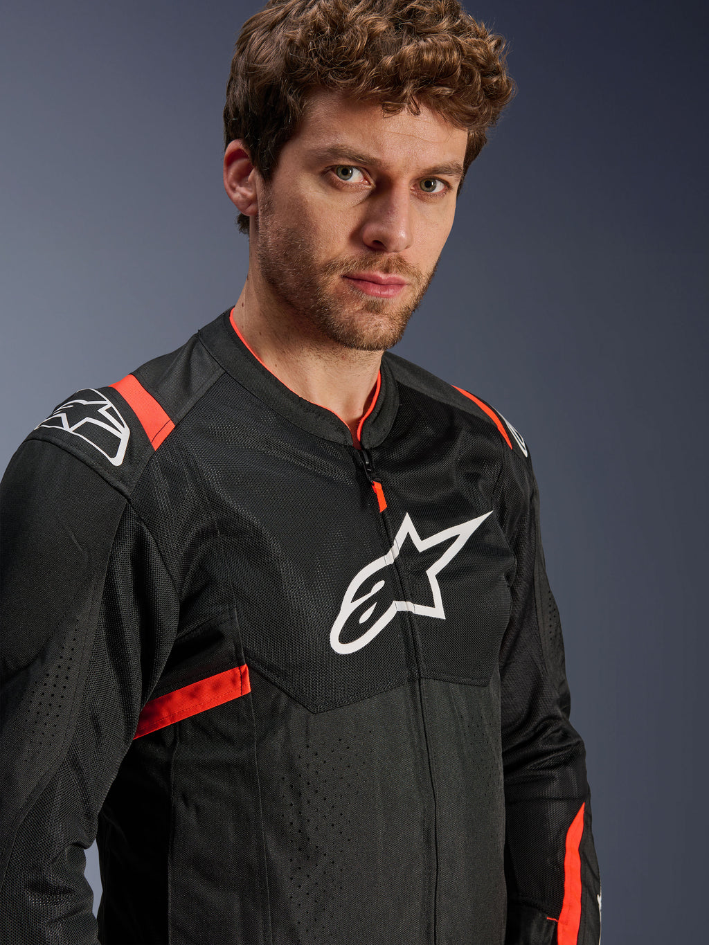 Alpinestars T-Sps Air V2 Jacke, Schwarz mit Red Fluo Akzenten, Textil-Mesh-Motorradjacke, von einem Modell getragen, mit weißem Alpinestars-Logo auf der Brust und den Schultern, atmungsaktive Mesh-Panels, sportlicher urbaner Fahrstil