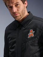 Alpinestars Ignite Air Jacke, Schwarz, mit traditionellem Hemdkragen und atmungsaktiver Mesh-Konstruktion, hervorgehoben durch einen rot-goldenen 'A'-Logo-Aufnäher auf der Brust, getragen von einem männlichen Model, urbane Motorradbekleidung