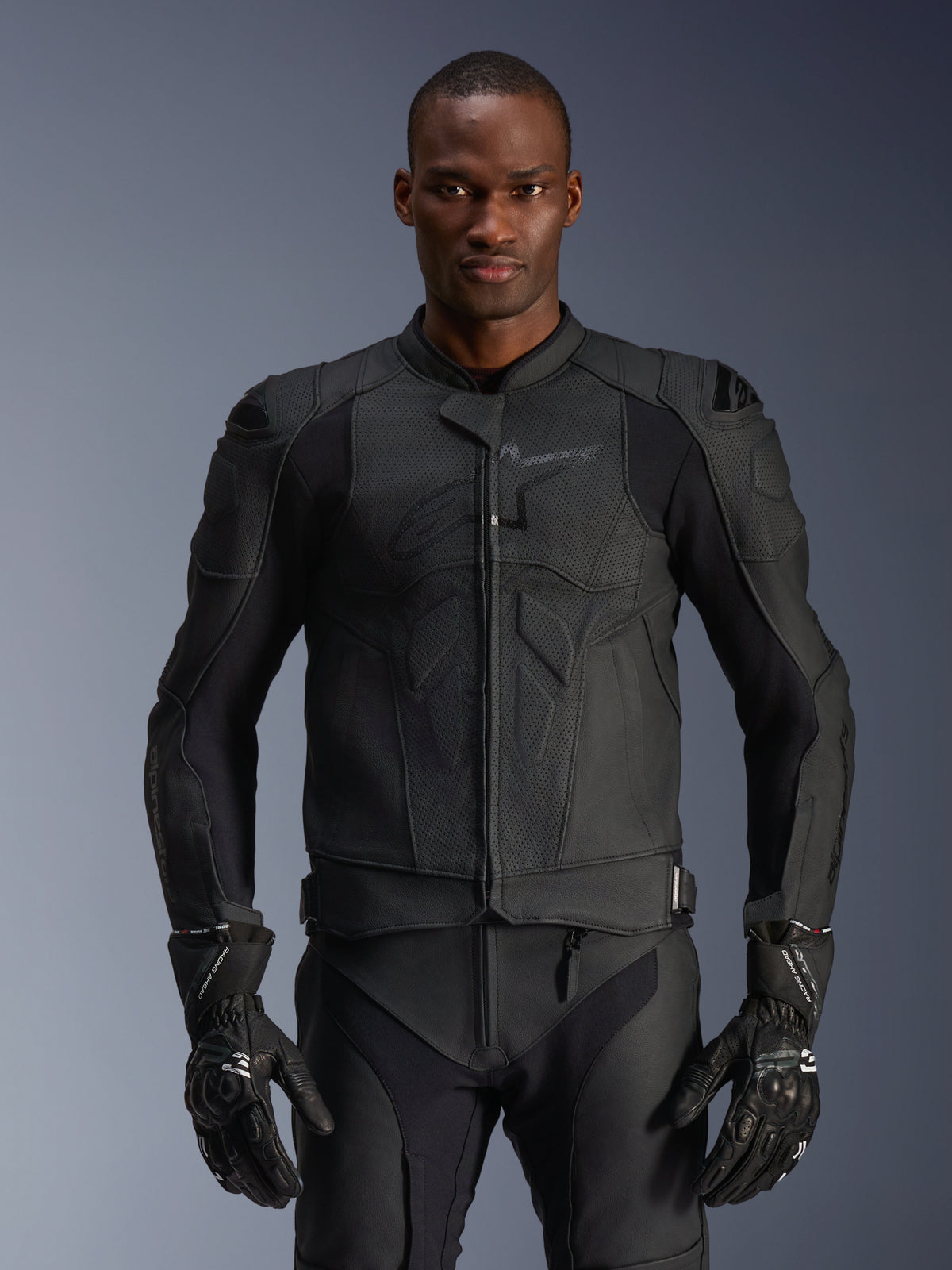 Alpinestars Dusk Airflow Leather Jacket, veste de moto noire, cuir perforé avec rembourrage de protection aux épaules, design ajusté, portée avec des gants de moto blindés noirs assortis