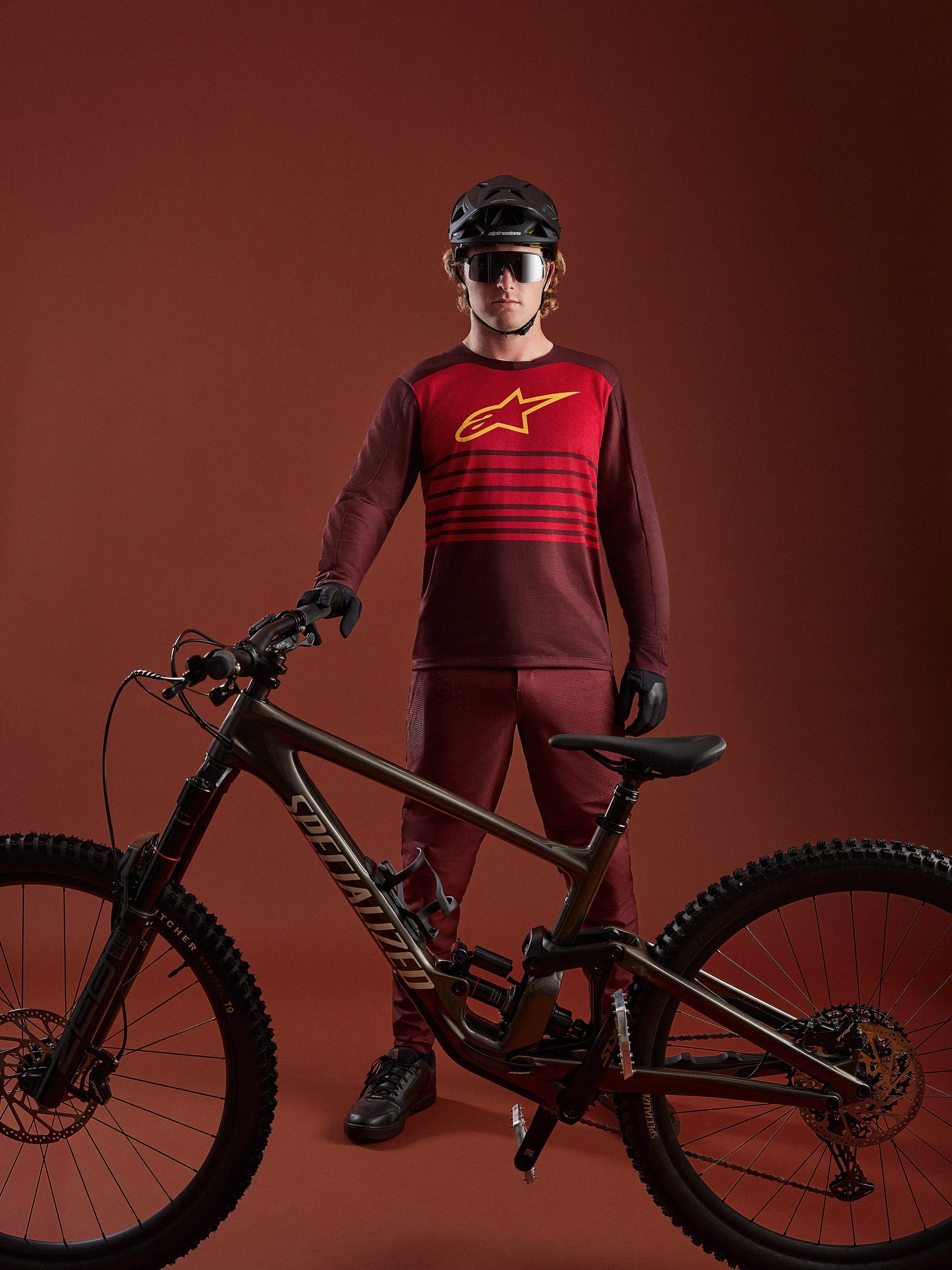 Bordeaux A-Dura Elite Trui 2.0 met lange mouwen, rood borstpaneel en geel logo, getoond met een mountainbike.