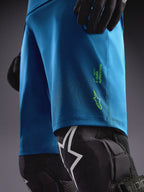 Short Alpinestars A-Dura Ride bleu-vert avec logos vert citron, associé à des genouillères pour le VTT.