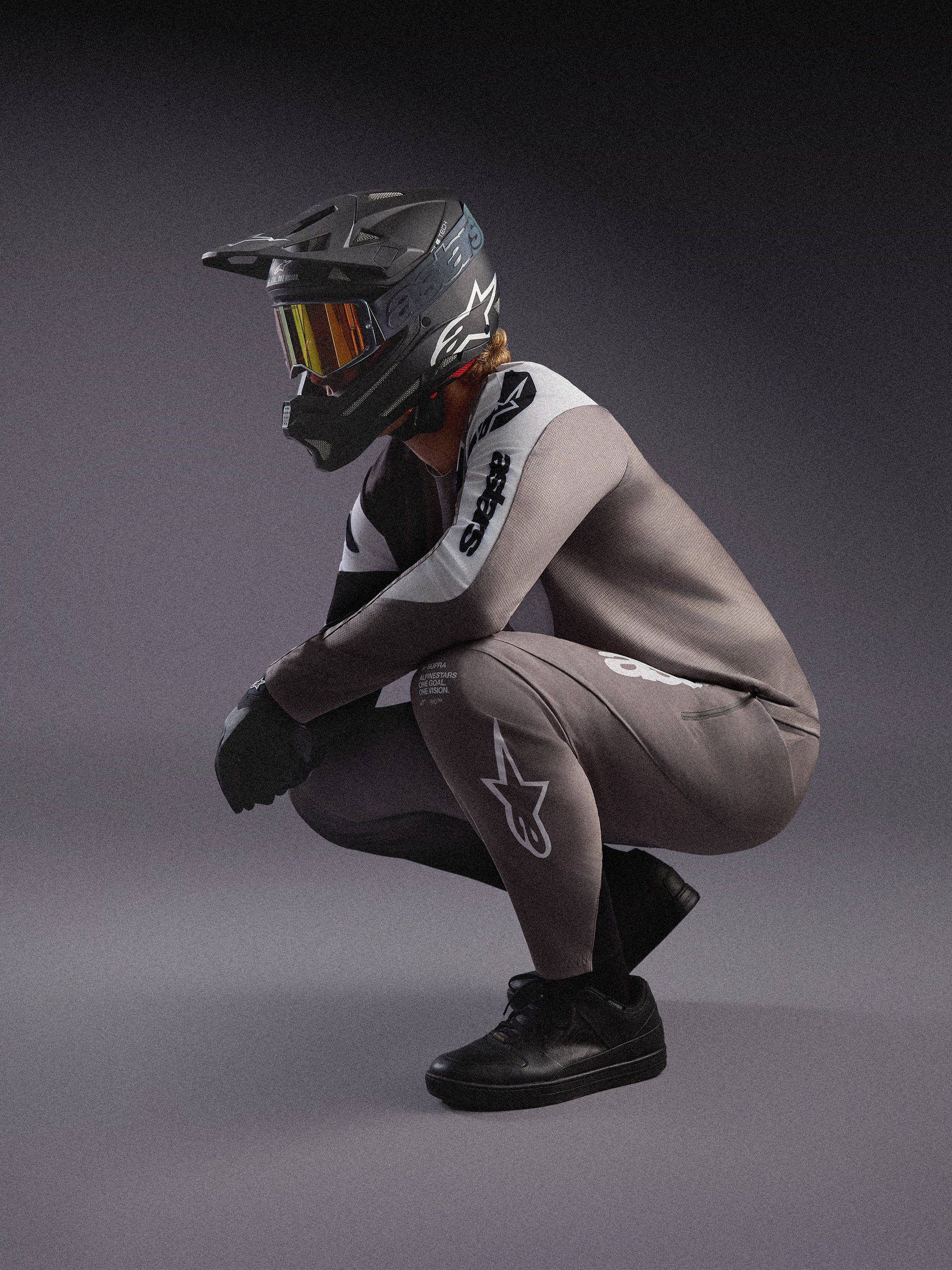 Ensemble VTT A-Supra Elite Alpinestars gris dégradé, maillot et pantalon avec casque intégral et masque de course noirs.