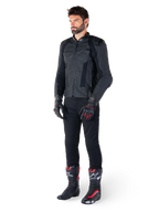 Veste en cuir Alpinestars Missile V3, noire, portée par un pilote avec un pantalon noir et des gants et bottes de course noirs et rouges, dotée de panneaux en cuir perforé et d'un logo monochrome élégant, esthétique sportive professionnelle