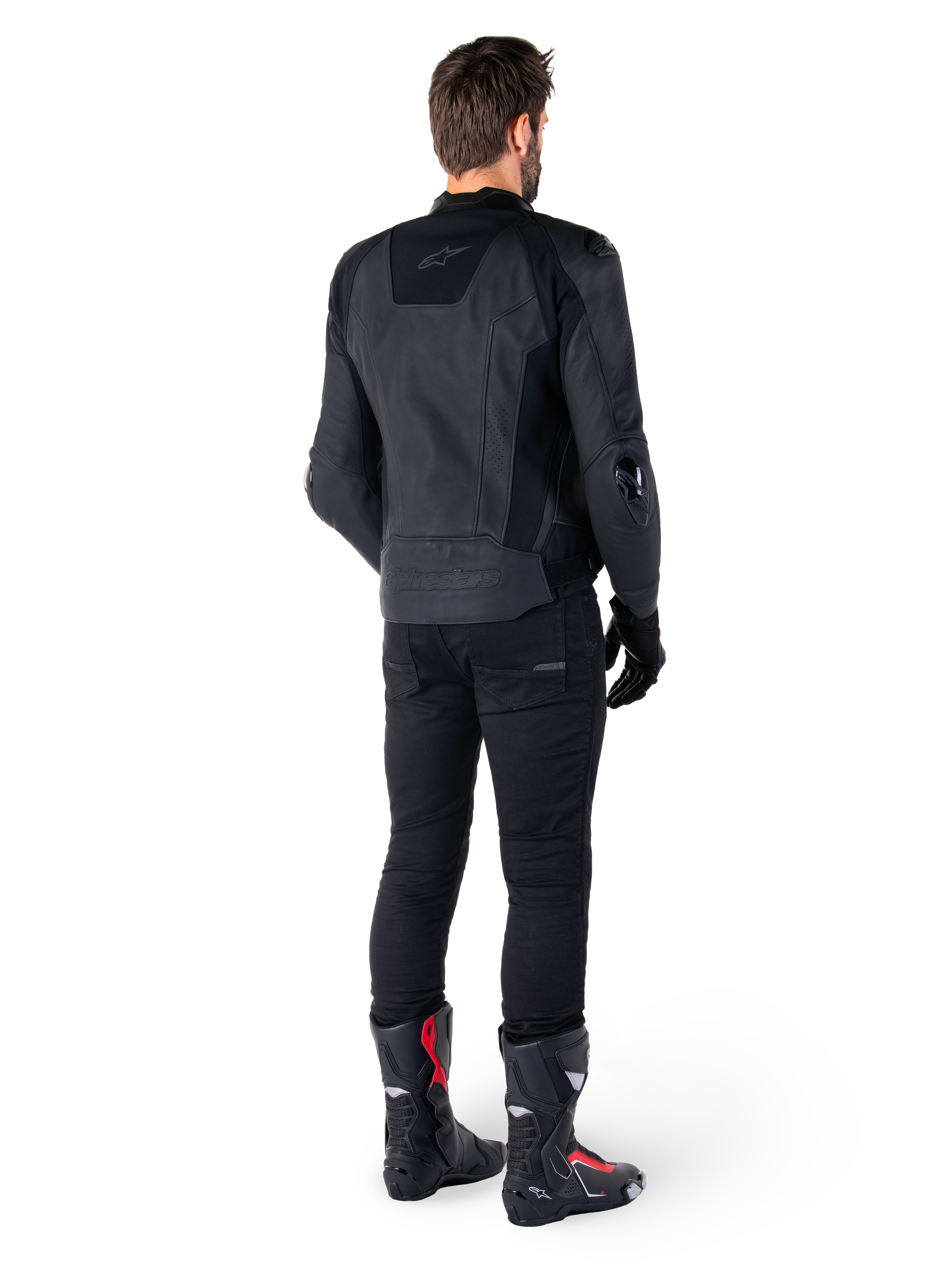 Veste en cuir Alpinestars Missile V3 noire, vue arrière sur un motard, portée avec un pantalon noir et des bottes de course noires et rouges, dotée d'une construction en cuir élégante avec un marquage ton sur ton et une coupe racing performante