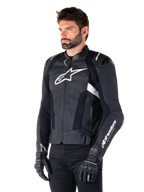 Veste en cuir Alpinestars Missile V3, noir et blanc, portée par un homme avec des gants de moto noirs, arborant un logo Alpinestars blanc proéminent sur la poitrine, des sliders d'épaules externes et des panneaux perforés pour un look d'inspiration racing.