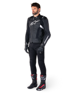 Motard portant la veste en cuir Alpinestars Missile V3 en noir et blanc, arborant un logo blanc sur la poitrine et des panneaux en cuir perforé, associée à un pantalon de moto noir, des gants noirs et des bottes de course noires et rouges pour un look de conduite sportive complet.