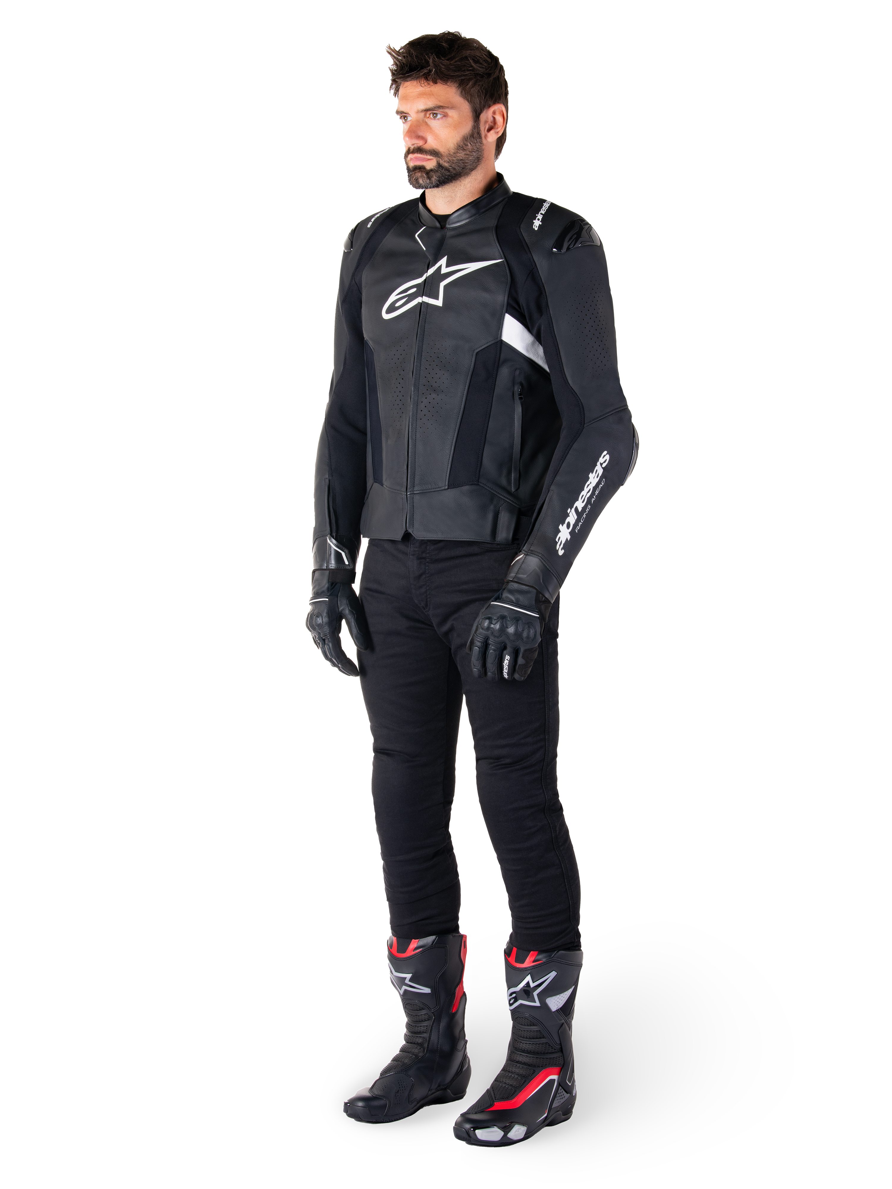 Motard portant la veste en cuir Alpinestars Missile V3 en noir et blanc, arborant un logo blanc sur la poitrine et des panneaux en cuir perforé, associée à un pantalon de moto noir, des gants noirs et des bottes de course noires et rouges pour un look de conduite sportive complet.