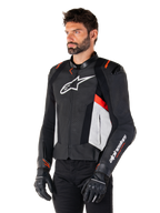 Alpinestars Missile V3 Leren Jas, zwart, wit en rood fluo, racing sport motorjas gedragen door een model met zwarte handschoenen en broek, voorzien van geperforeerde leren panelen en opvallende Alpinestars-branding