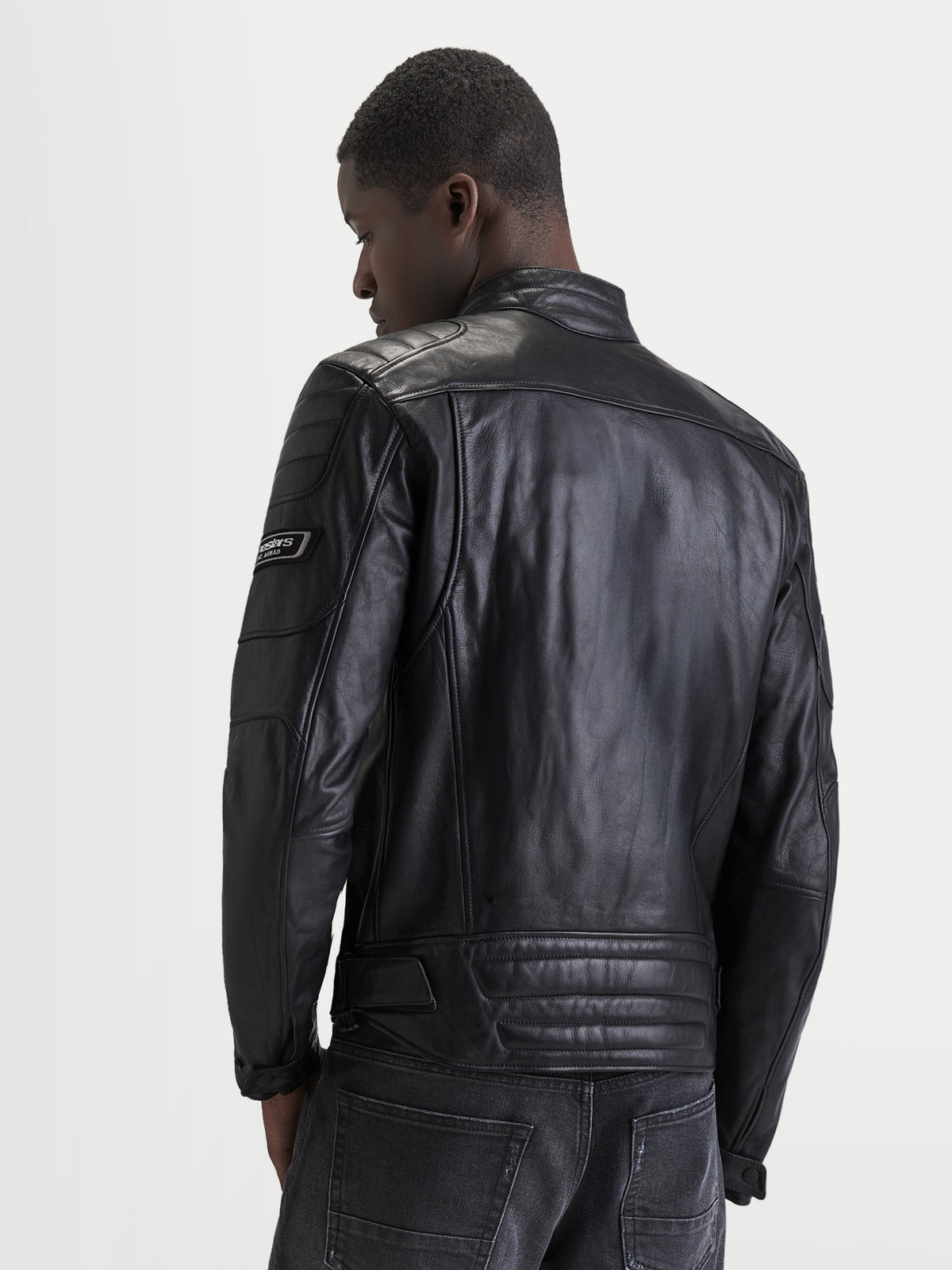 Alpinestars Revern Veste en cuir, blouson de moto en cuir noir pour homme, vue de dos sur un modèle montrant la construction en cuir bovin pleine fleur vieilli, le col motard classique et les détails de marquage de style heritage