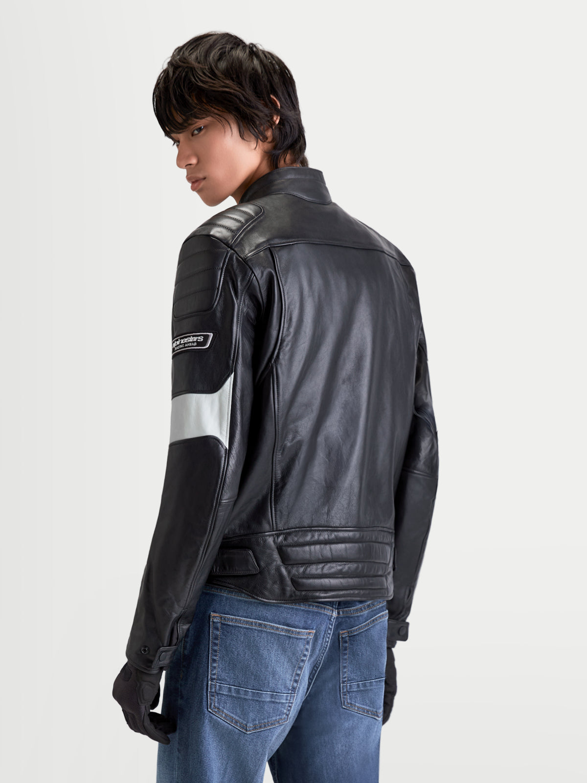 Alpinestars Revern Leren jas, stedelijke heren-motorjas van leer in het zwart en metaalgrijs, achteraanzicht op een model in spijkerbroek, met distressed rundleer en heritage-uitstraling