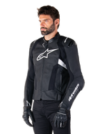 Mann in der Alpinestars Missile V3 Airflow Lederjacke, Motorradjacke in Schwarz und Weiß, hochwertiges perforiertes Leder für Luftzirkulation, weißes Alpinestars-Logo auf Brust und Ärmel, sportliche Passform im Rennsport-Stil, getragen mit schwarzen Handschuhen und Hose