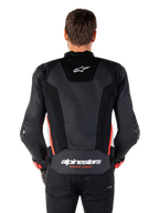 Rückansicht einer Person, die die Alpinestars Missile V3 Airflow Lederjacke in Schwarz Weiß Rot Fluo trägt, mit großflächigen perforierten Lederbahnen zur Belüftung, einem kleinen Alpinestars-Logo auf dem oberen Rücken und dem markanten „alpinestars RACING AHEAD“-Branding am unteren Taillenbereich.