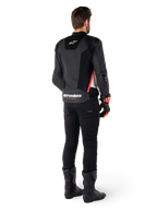 Rückansicht eines Fahrers mit der Alpinestars Missile V3 Airflow Lederjacke in Schwarz Weiß Rot Fluo, kombiniert mit schwarzer Hose und schwarzen Stiefeln, großflächig perforiertes Leder für Belüftung, DFS-Schulterprotektoren und markantes Alpinestars-Branding auf dem unteren Rücken.