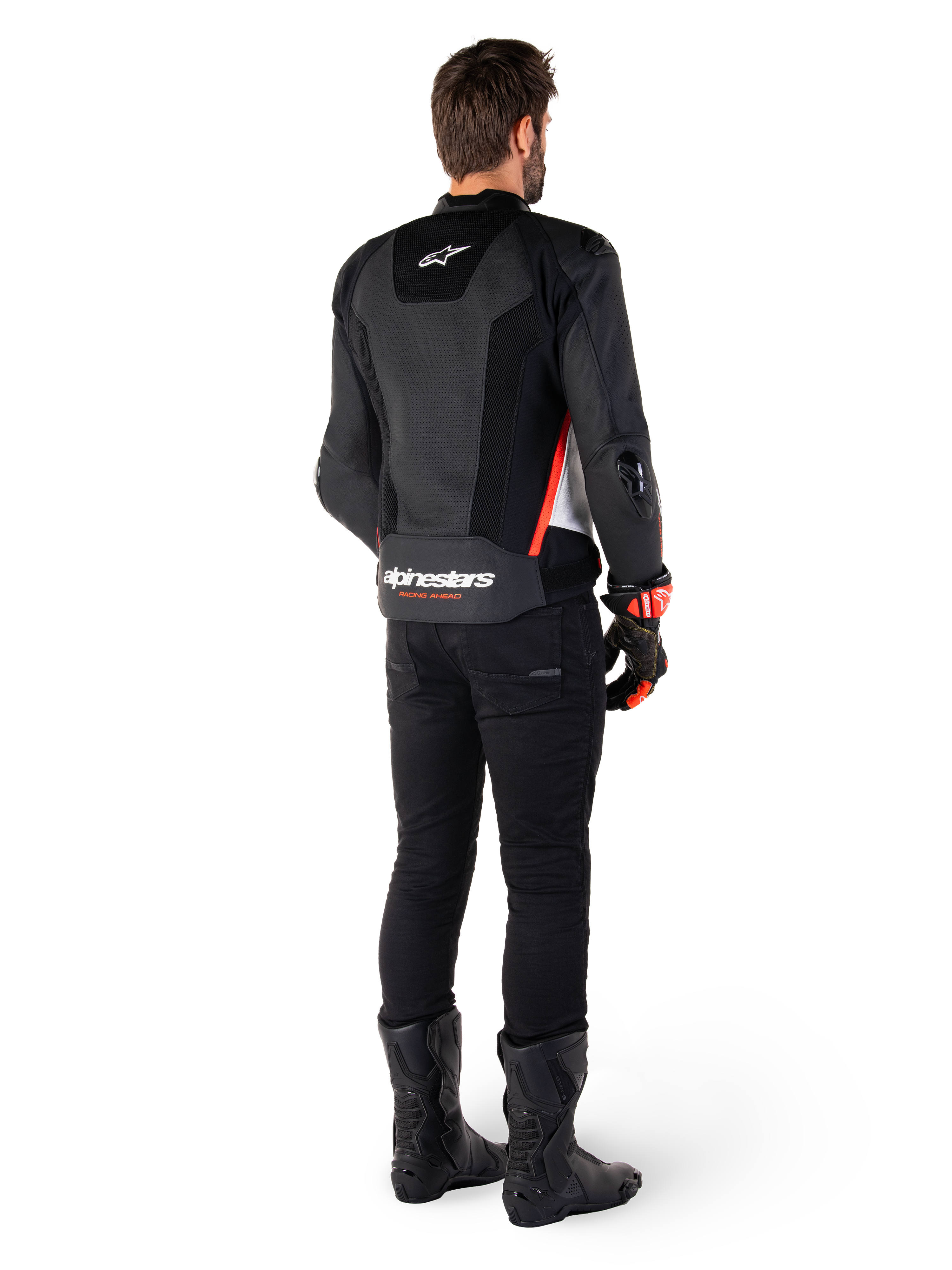 Rückansicht eines Fahrers mit der Alpinestars Missile V3 Airflow Lederjacke in Schwarz Weiß Rot Fluo, kombiniert mit schwarzer Hose und schwarzen Stiefeln, großflächig perforiertes Leder für Belüftung, DFS-Schulterprotektoren und markantes Alpinestars-Branding auf dem unteren Rücken.