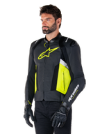 Männliches Model trägt Alpinestars Missile V3 Airflow Lederjacke, Schwarz mit Gelb Fluo und weißen Akzenten, mit perforiertem Leder für maximale Belüftung, markantes gelbes Logo auf der Brust, kombiniert mit schwarzen Handschuhen und Hosen, sportliche Racing-Motorradausrüstung
