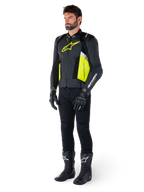 Männliches Model in der Alpinestars Missile V3 Airflow Lederjacke in Schwarz, Gelb Fluo und Weiß, kombiniert mit schwarzen Motorradhandschuhen, Hose und Stiefeln, zeigt das perforierte Lederdesign und die vom Rennsport inspirierte Ästhetik.