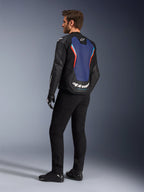 Dreiviertel-Rückansicht eines männlichen Models in der Alpinestars GP Force V2 Lederjacke in Schwarz Blau Rot Fluo, die das blaue Rückenpanel mit roten fluoreszierenden Akzenten und weißem Branding hervorhebt, kombiniert mit einer schwarzen Hose und Motorradhandschuhen.