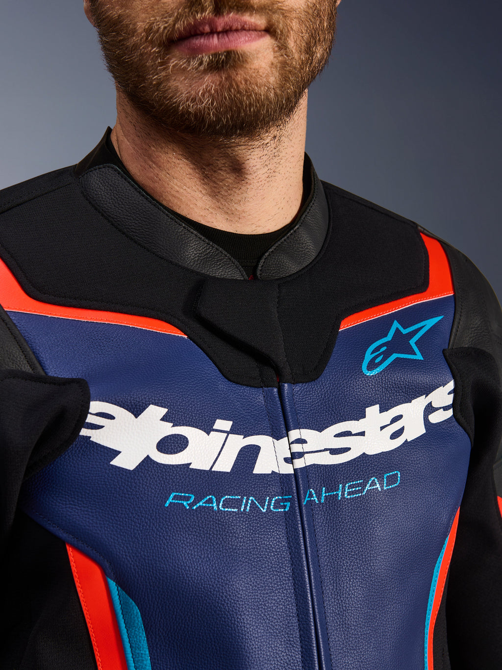 Alpinestars GP Force V2 Lederjacke, Detailansicht von Brust und Kragen, Blau, Schwarz und Rot Fluo, mit weißem Alpinestars-Logo und hellblauem 'RACING AHEAD'-Schriftzug, hochwertige Lederstruktur mit fluoreszierenden Akzenten