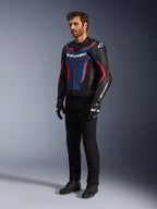 Model trägt die Alpinestars GP Force V2 Lederjacke in Schwarz Blau Rot Fluo, kombiniert mit schwarzer technischer Fahrhose, schwarzen Handschuhen und Stiefeln, professionelle Motorrad-Rennausrüstung für sportliches Fahren