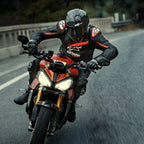 Motorradfahrer auf einem roten Sportmotorrad, Alpinestars GP Plus R V4 Rideknit Lederjacke, Schwarz mit fluoroten und weißen Details, mit weißem Alpinestars-Logo und „ASTARS“-Schriftzug, kombiniert mit schwarzem Rennhelm und Handschuhen, Performance-Fahrausrüstung in Aktion auf einer Straße.