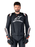 Alpinestars Missile V3 Ignition Lederjacke, Schwarz mit weißen und roten Akzenten, getragen von einem männlichen Model mit passenden Rennhandschuhen und -hose, aus der MotoGP abgeleitete Sport-Motorradjacke mit markantem Branding