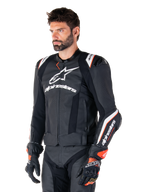 Männliches Model trägt die Alpinestars Missile V3 Ignition Lederjacke, Schwarz mit weißen und orangefarbenen Akzenten, markante weiße Logos, perforierte Lederbereiche und Schulterprotektoren, kombiniert mit Rennhandschuhen für einen sportlichen Racing-Look.