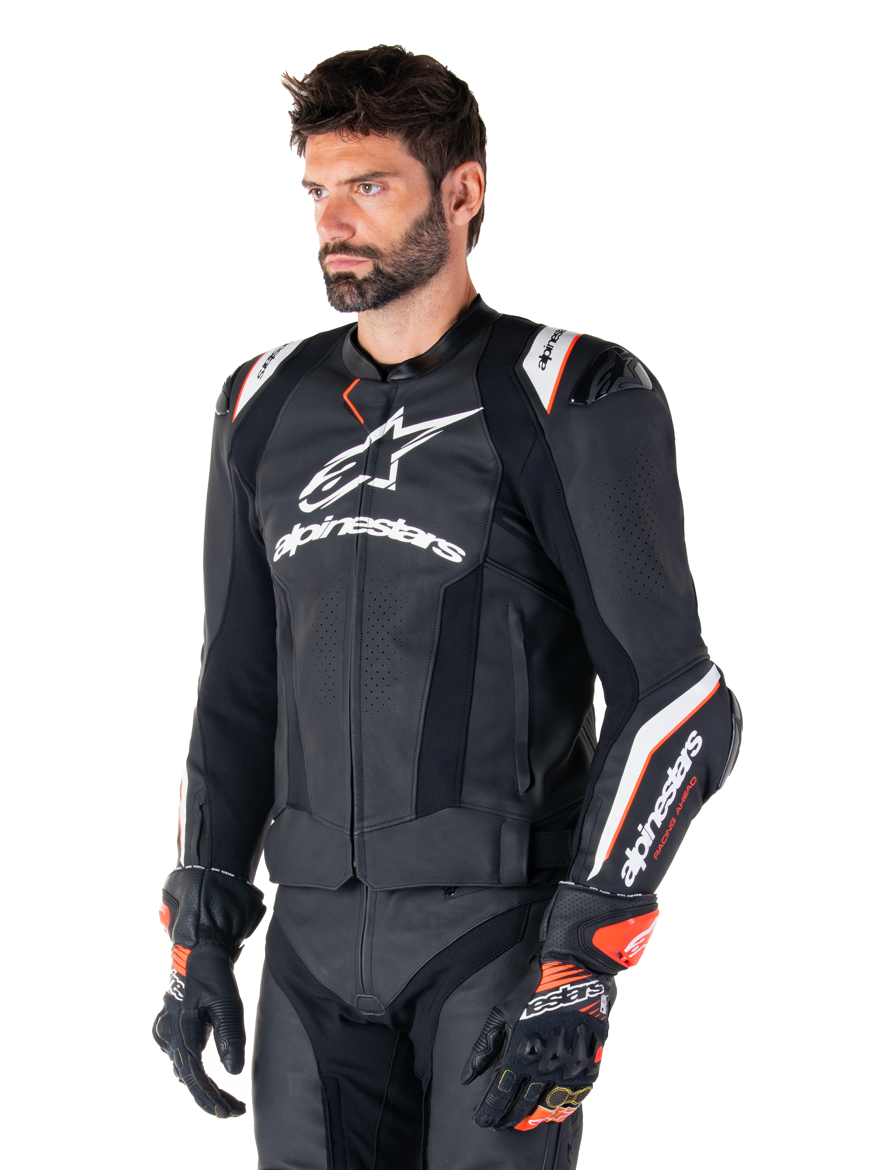 Männliches Model trägt die Alpinestars Missile V3 Ignition Lederjacke, Schwarz mit weißen und orangefarbenen Akzenten, markante weiße Logos, perforierte Lederbereiche und Schulterprotektoren, kombiniert mit Rennhandschuhen für einen sportlichen Racing-Look.