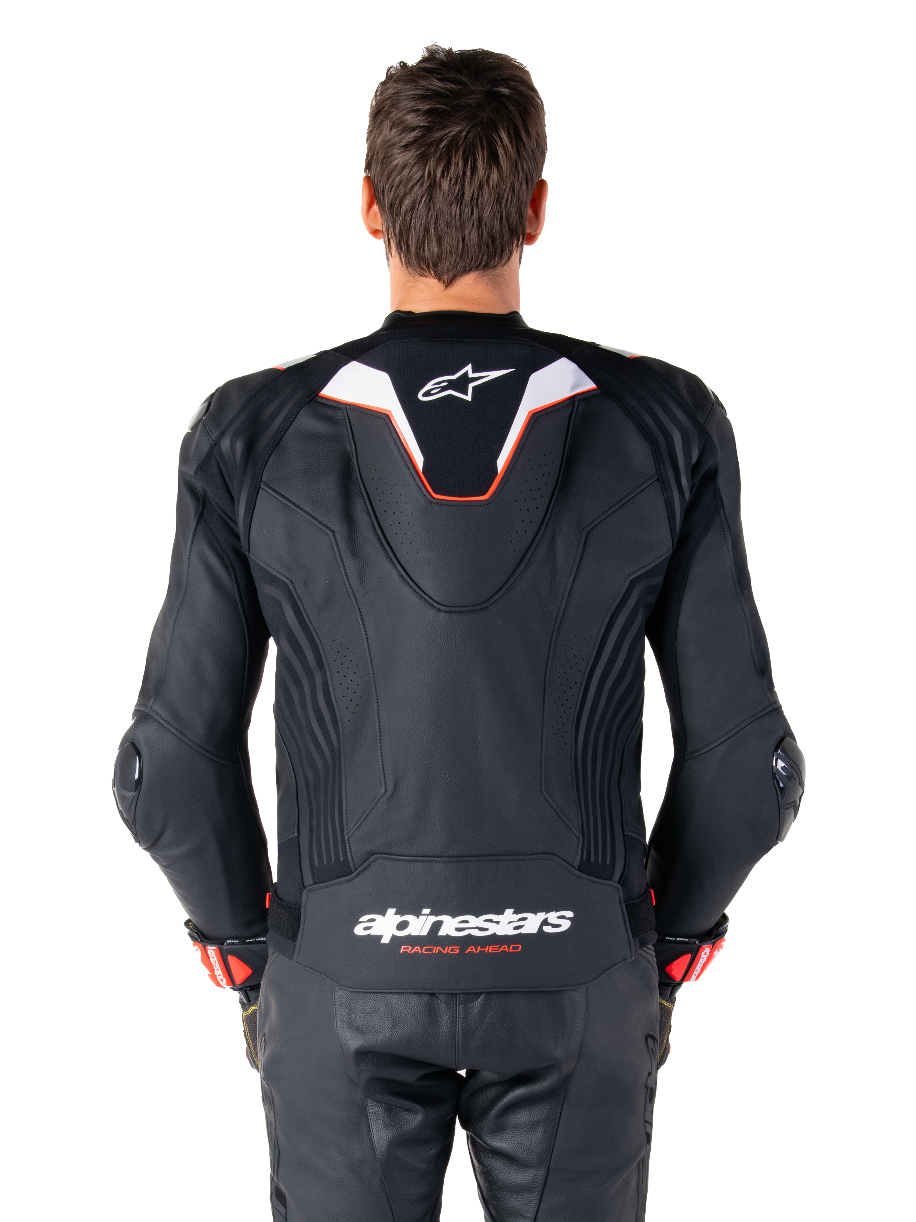Rückansicht eines Fahrers in der Alpinestars Missile V3 Ignition Lederjacke, schwarzes Leder mit weißen und roten Akzenten, schmaler Sport-Aero-Höcker mit weißem Logo und 'alpinestars RACING AHEAD' Branding auf dem unteren Rücken, kombiniert mit passender schwarzer Leder-Rennhose und Handschuhen.