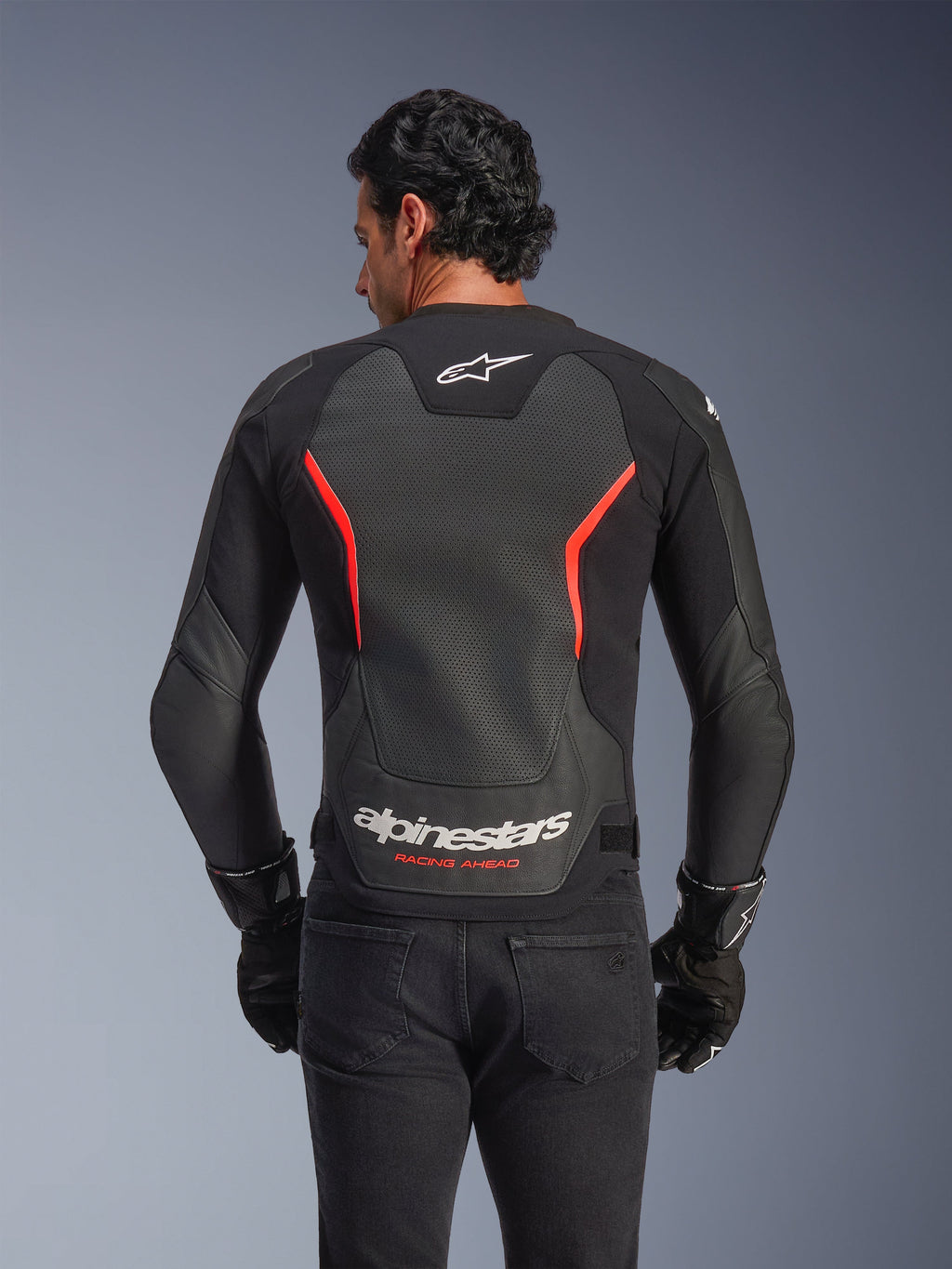 Alpinestars GP Force V2 Air Lederjacke, Rückansicht, Schwarz und Rot Fluo, mit einem großen perforierten Leder-Rückeneinsatz zur Belüftung, 'Alpinestars Racing Ahead'-Branding am unteren Rücken, getragen von einem Fahrer mit schwarzen Handschuhen, Performance-Sport-Motorradausrüstung