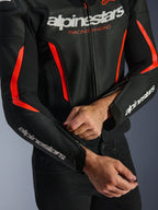 Alpinestars GP Force V2 Air Lederjacke in Schwarz und Rot Fluo, Nahaufnahme der perforierten Lederkonstruktion, weißes Branding auf Brust und Ärmeln, ein Fahrer passt den Unterarm-Reißverschluss für eine individuelle Passform an.